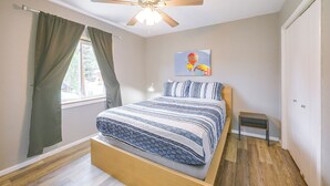 A bedroom with a bed, a ceiling fan, a window with curtains, a painting on the wall, and a small bedside table. - Walk to Ski Lifts! Apt in Heart of Red River (Red River)
