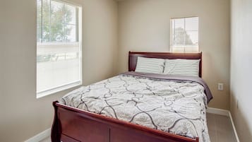 A bedroom with a wooden bed, a patterned bedspread, and two windows with blinds.