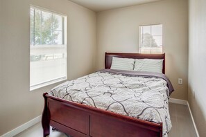 A bedroom with a wooden bed, a patterned bedspread, and two windows with blinds.