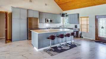 A modern kitchen with grey cabinets, a stainless steel refrigerator, a microwave, and a large island with bar stools.
