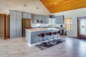Eine moderne Küche mit grauen Schränken, einem Edelstahl-Kühlschrank, einer Mikrowelle und einer großen Kochinsel mit Barhocker.