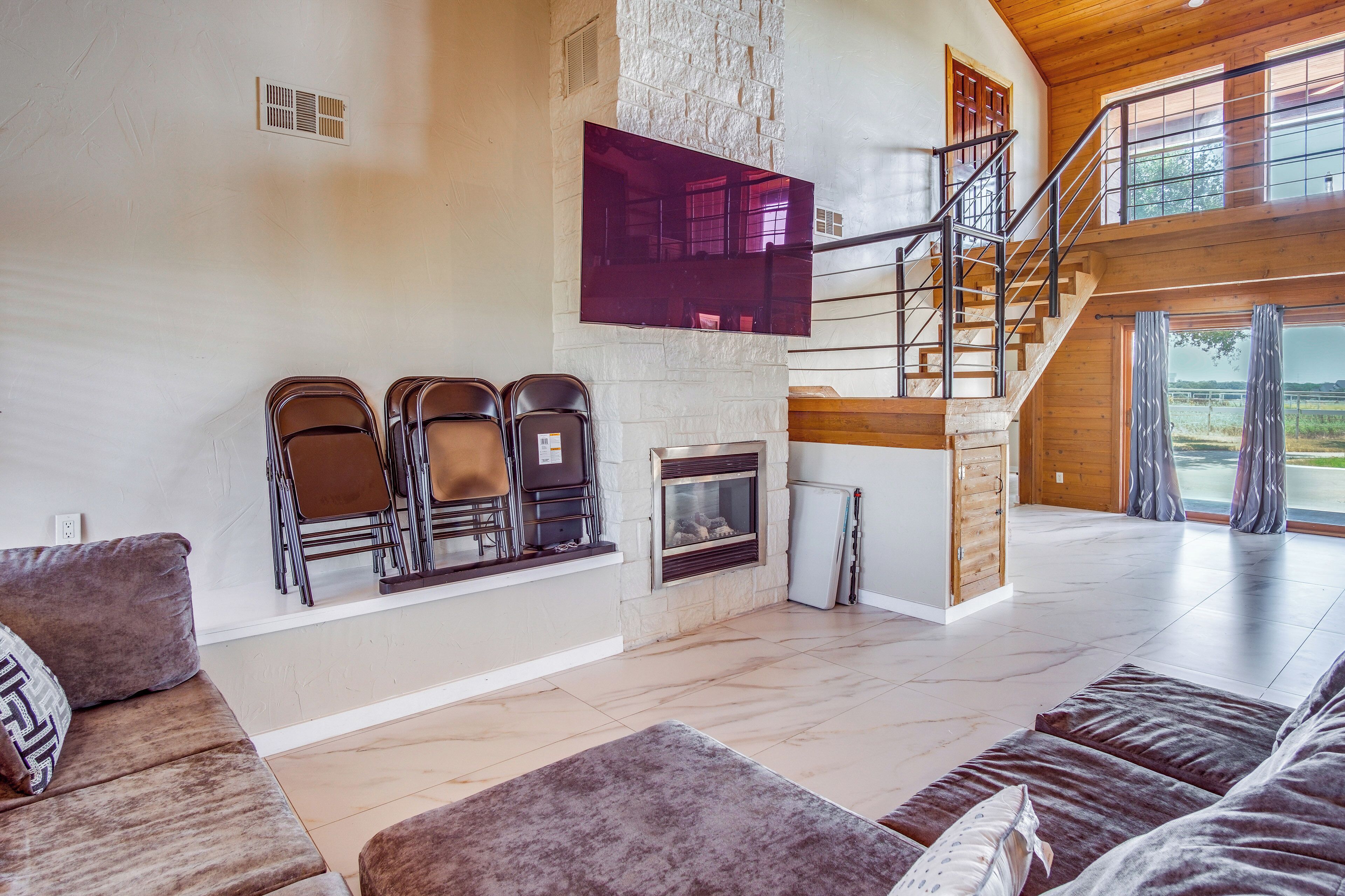 A spacious living room with a fireplace, a staircase, and a large window offering a view of the outdoors.