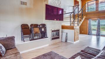 A spacious living room with a fireplace, a staircase, and a large window offering a view of the outdoors.