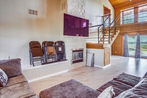 A spacious living room with a fireplace, a staircase, and a large window offering a view of the outdoors.
