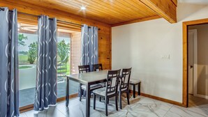 A dining area with a table and chairs, wooden ceiling, and a view through the curtains. - Gated Ranch Retreat Near Lakes & Frisco (Aubrey)