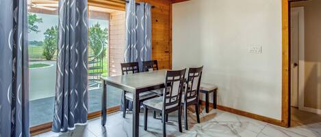 A dining area with a table and chairs, wooden ceiling, and a view through the curtains.