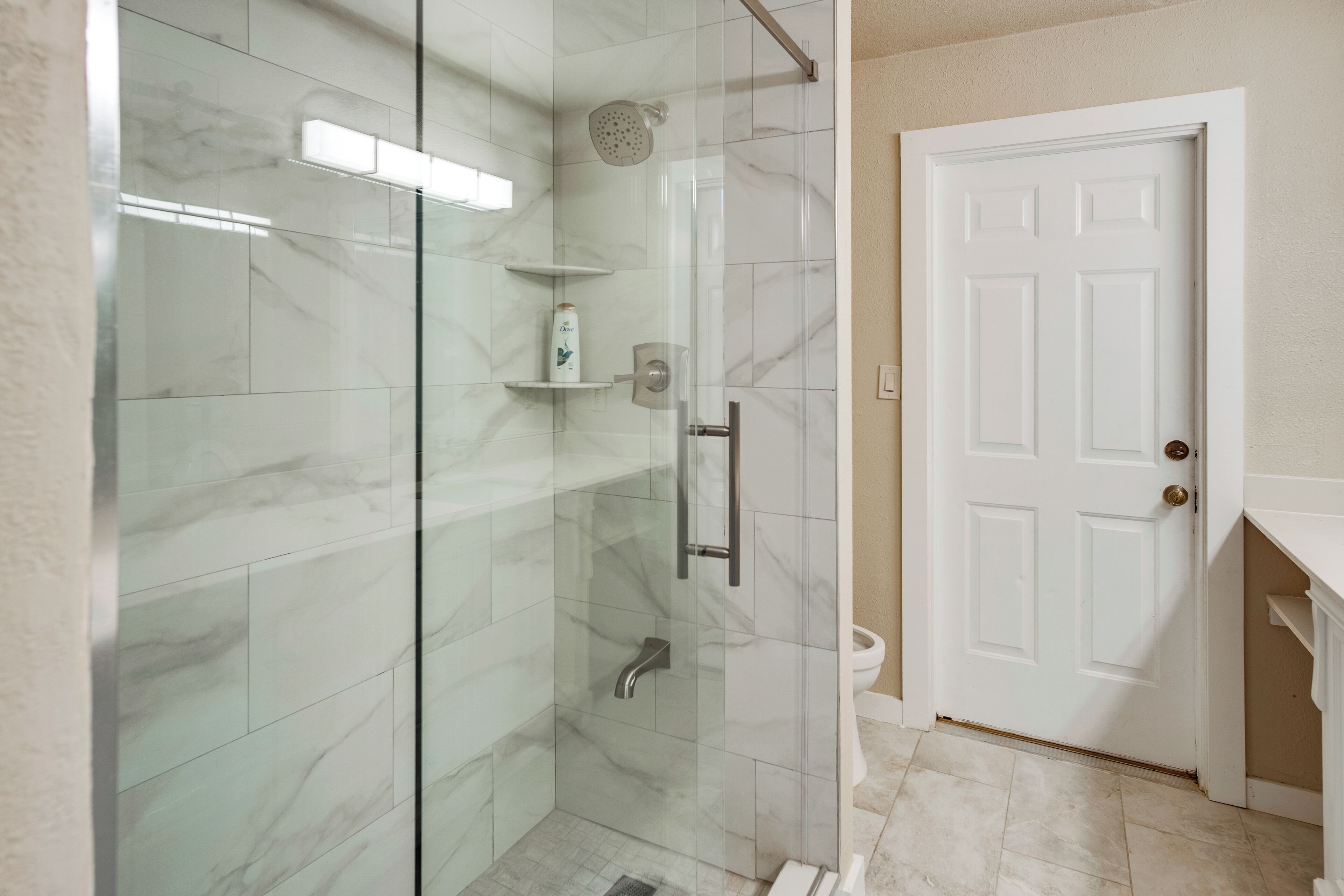A modern bathroom with a glass-enclosed shower, a white door, and marble tiles.