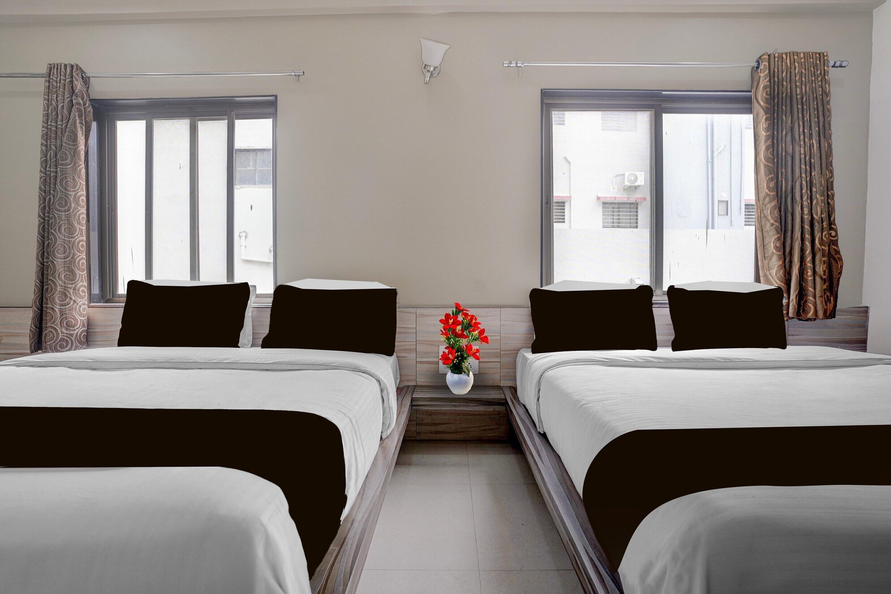 A hotel room with two beds, a small table with a vase of flowers, and a window with curtains.
