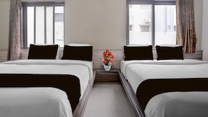 A hotel room with two beds, a small table with a vase of flowers, and a window with curtains.