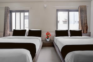 A hotel room with two beds, a small table with a vase of flowers, and a window with curtains.