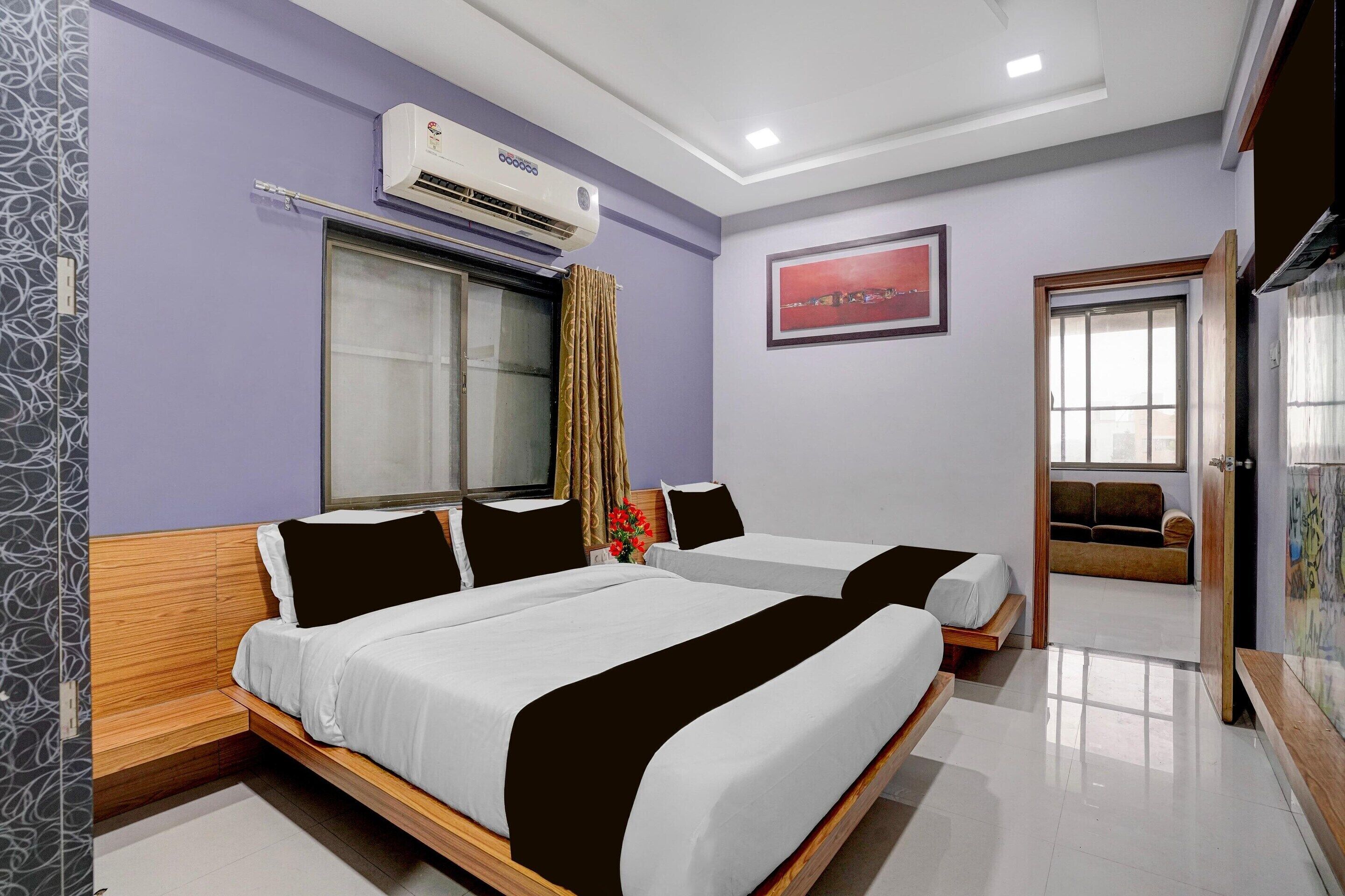 A hotel room with two beds, an air conditioning unit, a window with curtains, a framed picture on the wall, and a door leading to another room.