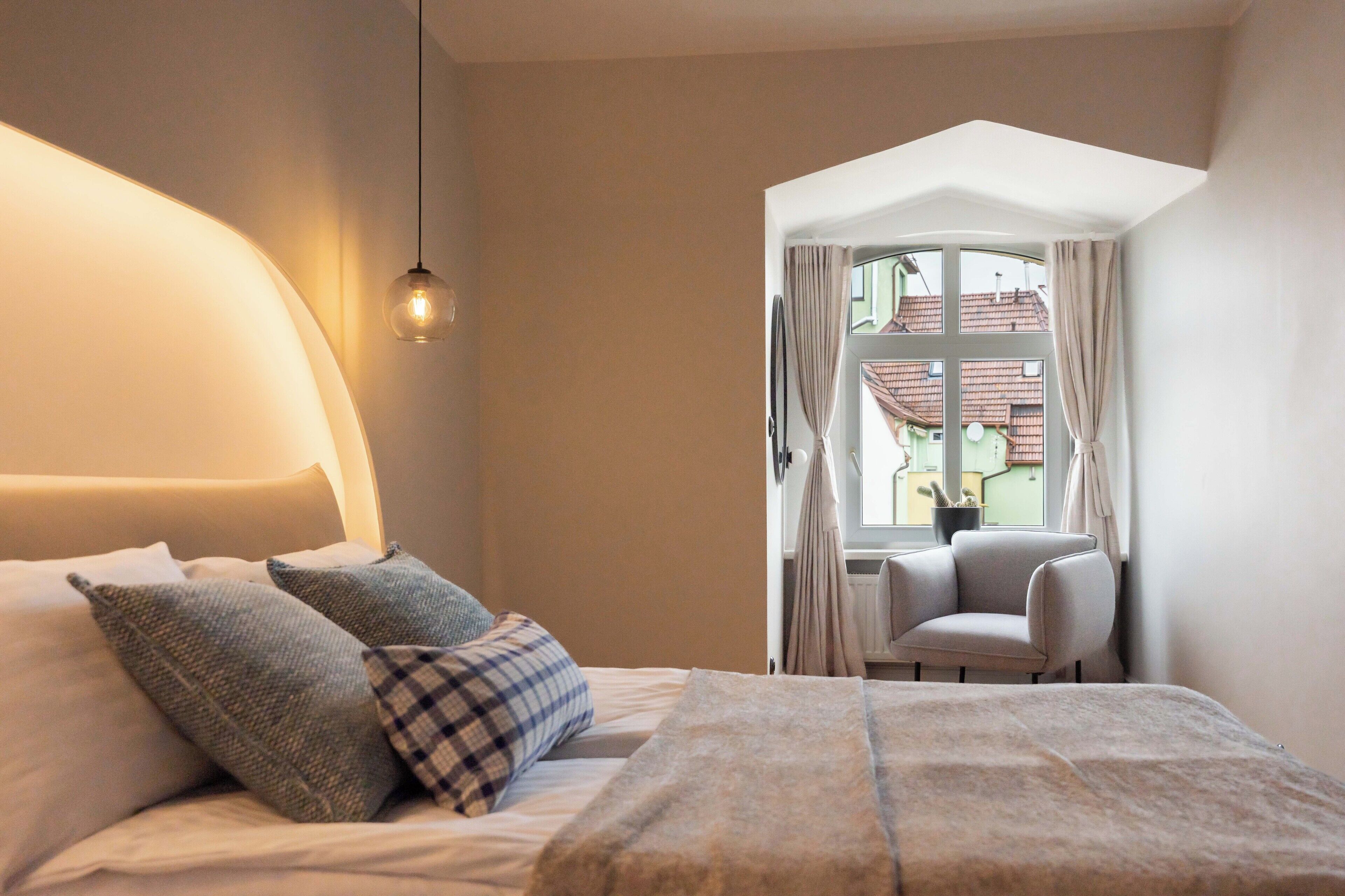 A bedroom with a bed, pillows, a chair, and a window with curtains.