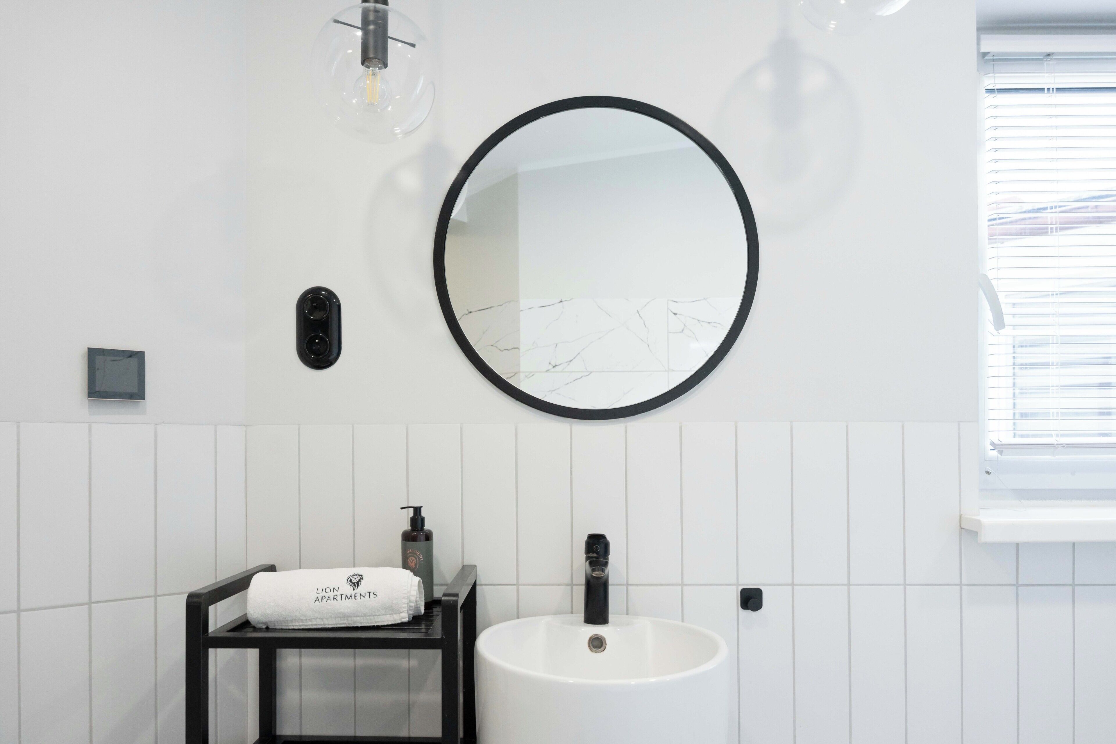 A bathroom with a round mirror, a white sink, a towel, and a soap dispenser.