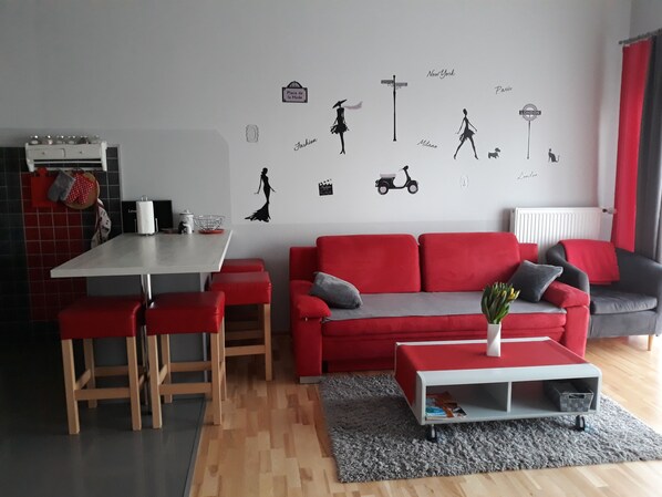 Ein modernes Wohnzimmer mit einem roten Sofa, einem grauen Sofa, einem weißen Esstisch und einem grauen Teppich.