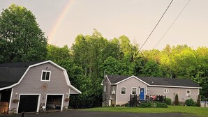Una proprietà rurale con un vialetto sterrato che conduce a una stalla e a una casa, immersa nel verde con un arcobaleno ben visibile.