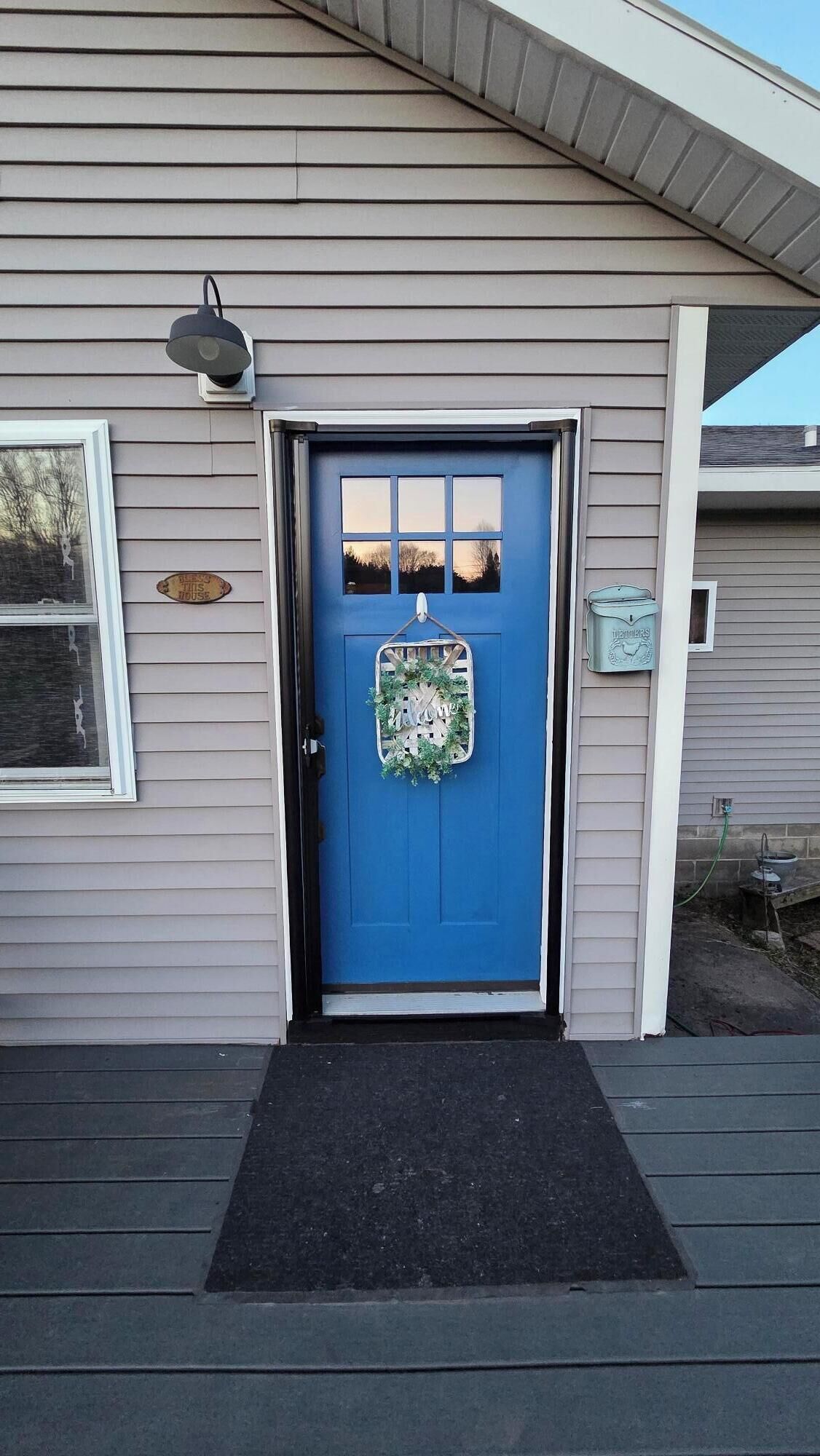 A house with a blue front door, a welcome sign, and a mailbox.
