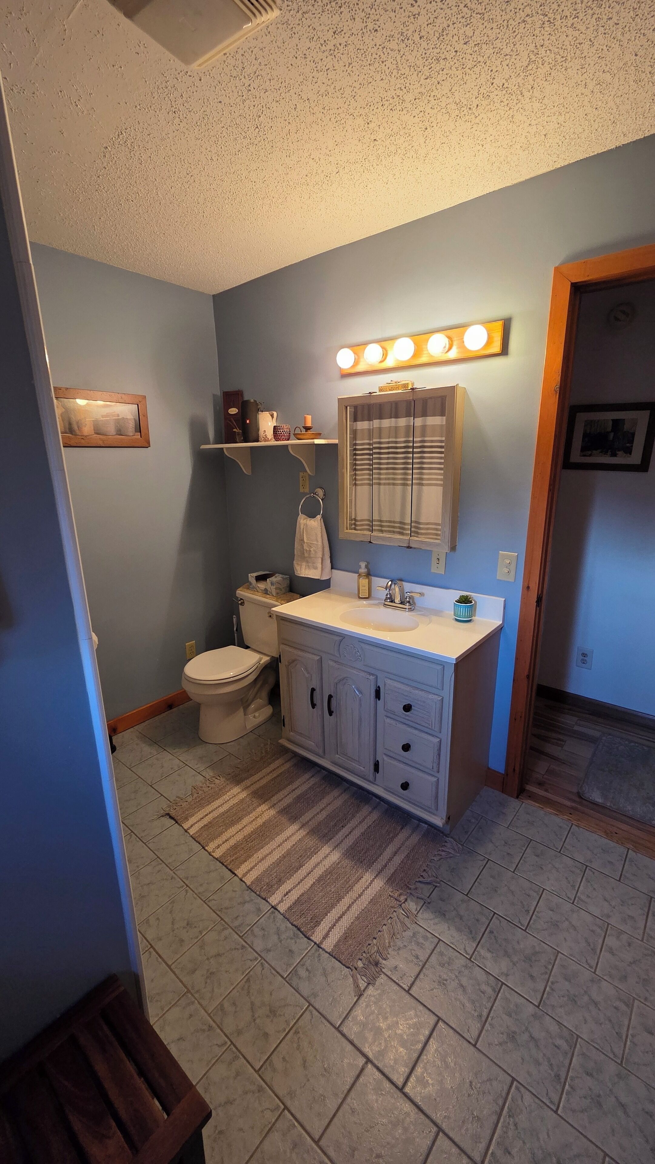 A bathroom with a toilet, sink, vanity, and a mirror with lights.