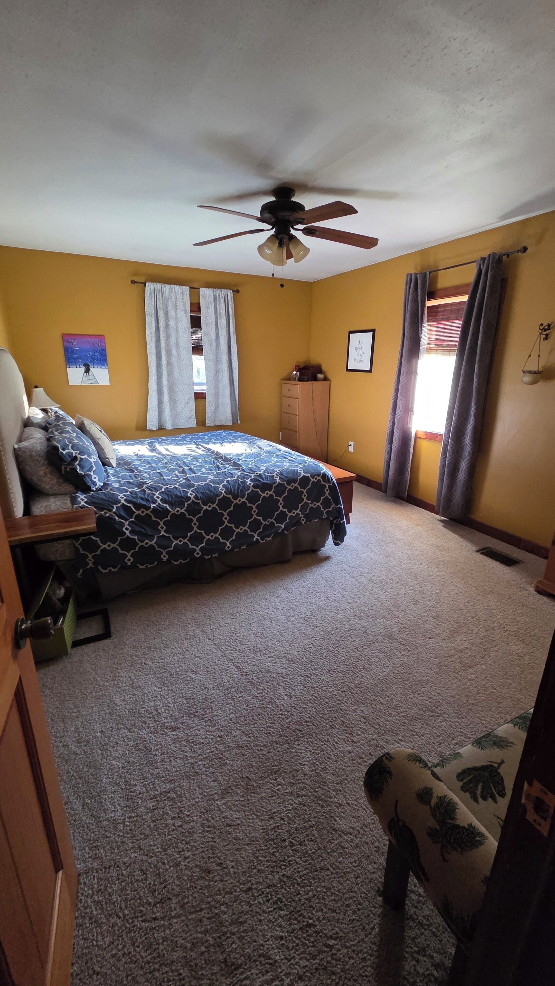 A bedroom with a bed, a ceiling fan, a window with curtains, and a small bedside table.