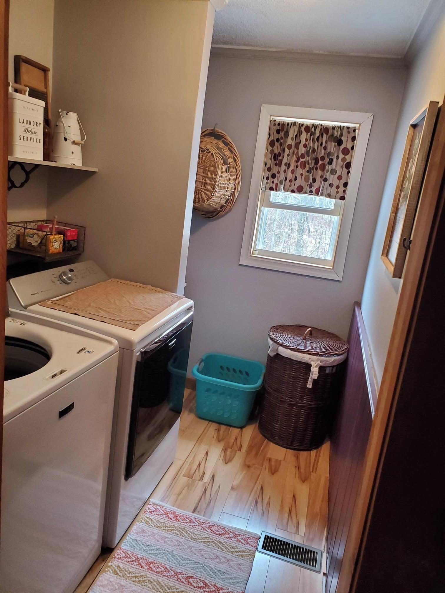 A laundry room with a washing machine, a dryer, a window with curtains, and a small basket.