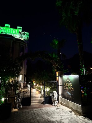 Entrada de un hotel con un letrero que dice 'GREEN GARDEN HOTEL' y una estatua de león.