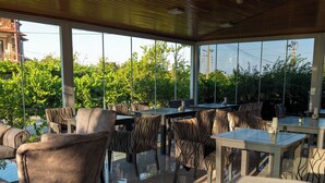 An outdoor seating area with tables and chairs, large windows, and a view of greenery. - Green Garden Göynük Hotel  (Kemer)