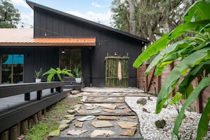 A modern building with a dark facade, a wooden deck, and a stone pathway leading to a bamboo gate. - Hidden Sanctuary with Heated Saltwater pool, fire pit, and koi pond (St. Augustine)