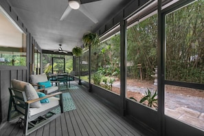 A covered outdoor seating area with a ceiling fan, a table with chairs, and a view of a garden. - Hidden Sanctuary with Heated Saltwater pool, fire pit, and koi pond (St. Augustine)