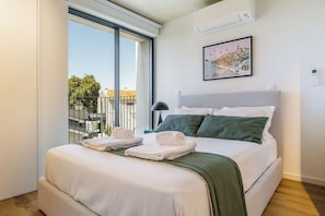 Ein Hotelzimmer mit einem Bett, einem Fenster mit Blick auf Gebäude, einem gerahmten Bild an der Wand und einem Thermostat.