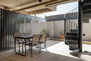 Une terrasse extérieure avec une table et des chaises, un escalier en colimaçon et une clôture en métal.