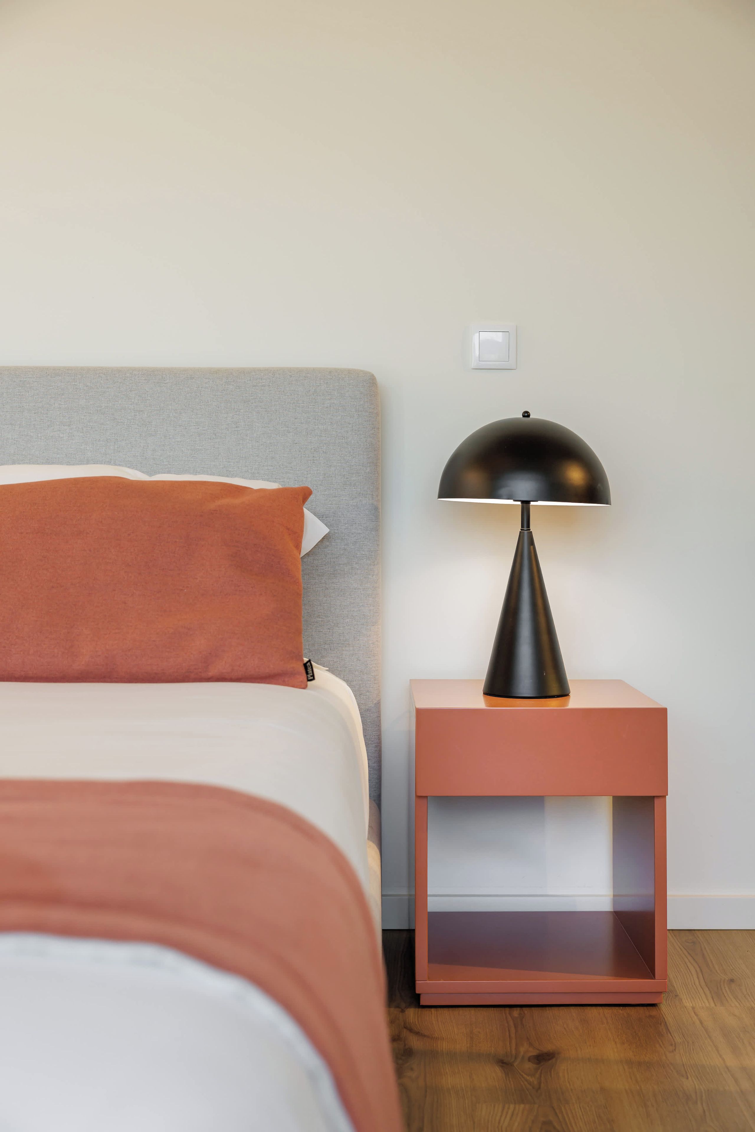 Ein Schlafzimmer mit einem Bett, einem Nachttisch, einer Lampe und einem Lichtschalter.