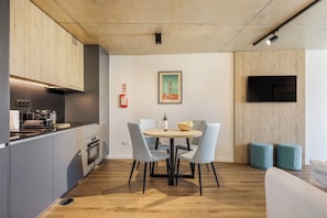 A modern kitchen with a dining area, a flat-screen TV mounted on the wall, and a framed picture of a cityscape. - Afurada Studio w/ Marina & Douro Views, Near Beach (Vila Nova de Gaia)