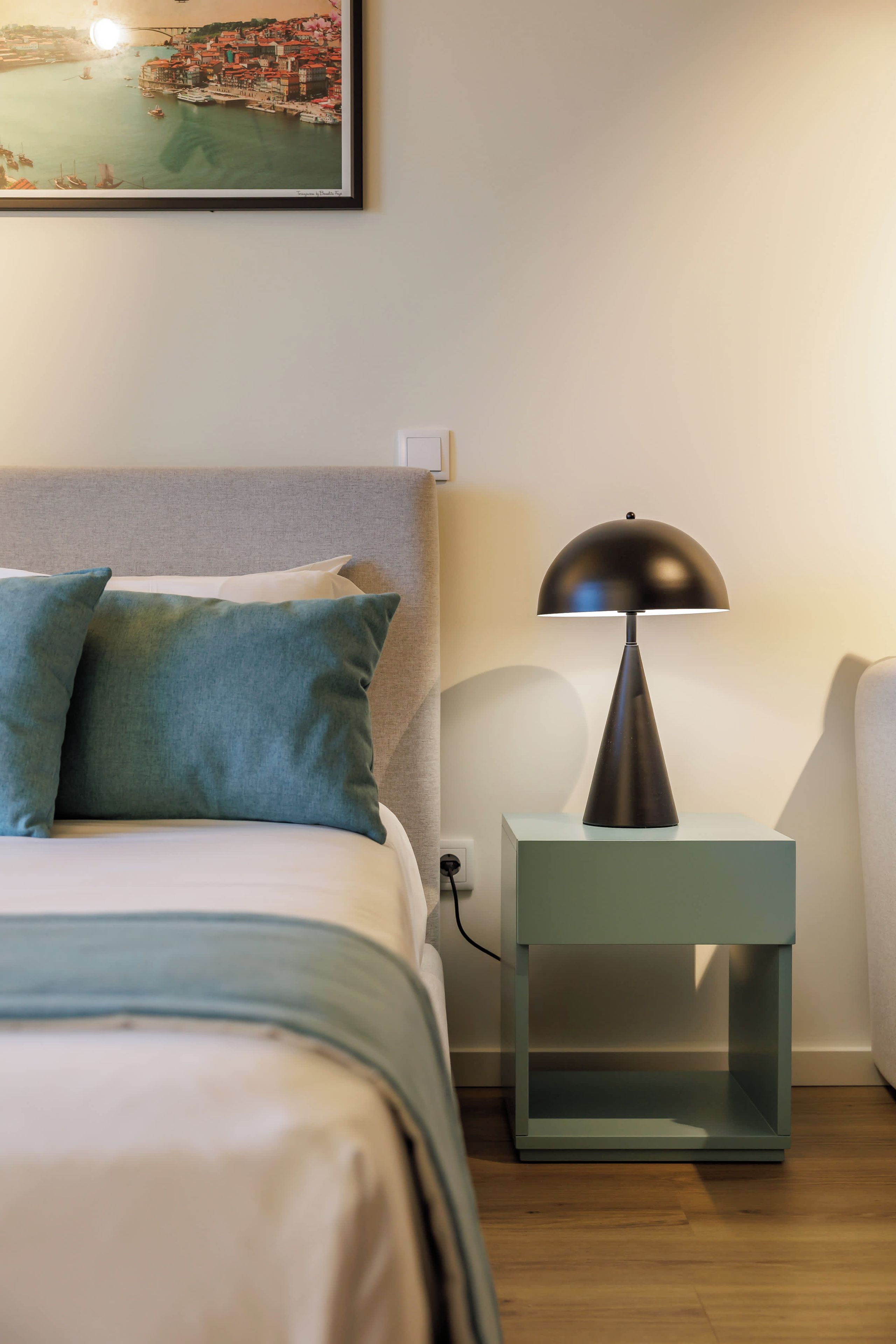 A neatly made bed with pillows, a bedside table with a lamp, and a framed picture on the wall.