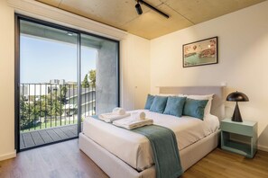 A bedroom with a bed, a nightstand, a lamp, a painting, and a balcony with a view. - Marina da Afurada Apartments - Miguel Cervantes (Vila Nova de Gaia)