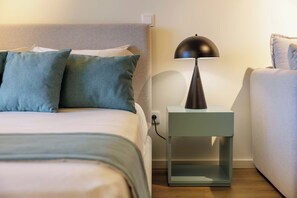 A neatly made bed with a grey headboard, a small bedside table with a lamp, and a wall socket. - Marina da Afurada Apartments - Miguel Cervantes (Vila Nova de Gaia)