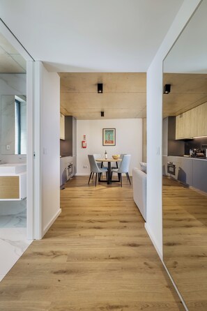 A modern kitchen with wooden cabinets, a dining area with a table and chairs, and a hallway with a wooden floor. - Marina da Afurada Apartments - Miguel Cervantes (Vila Nova de Gaia)