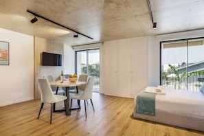 A modern hotel room with a dining area, a bed with a view, and a television on the wall. - Stylish Waterfront Apt Near Douro, Dining, & Beach (Vila Nova de Gaia)