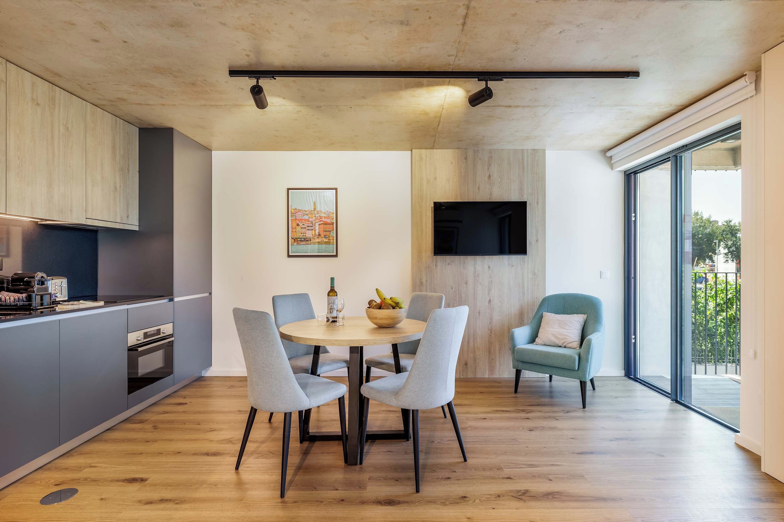 Una cocina moderna con electrodomésticos integrados, una zona de comedor con una mesa redonda y sillas, y un amplio ventanal con vistas al exterior.