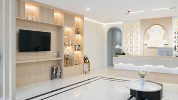 Un área de recepción moderna con un televisor de pantalla plana, mostrador de recepción y una pared decorativa con un diseño geométrico.