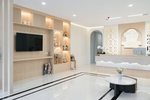 A modern reception area with a flat-screen TV, a reception desk, and a decorative wall with a geometric pattern. - Chochana Hometel Phuket Old Town (Phuket)