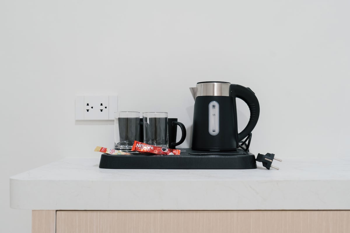 A black electric kettle on a white countertop with two glasses and a packet of Nescafe instant coffee.