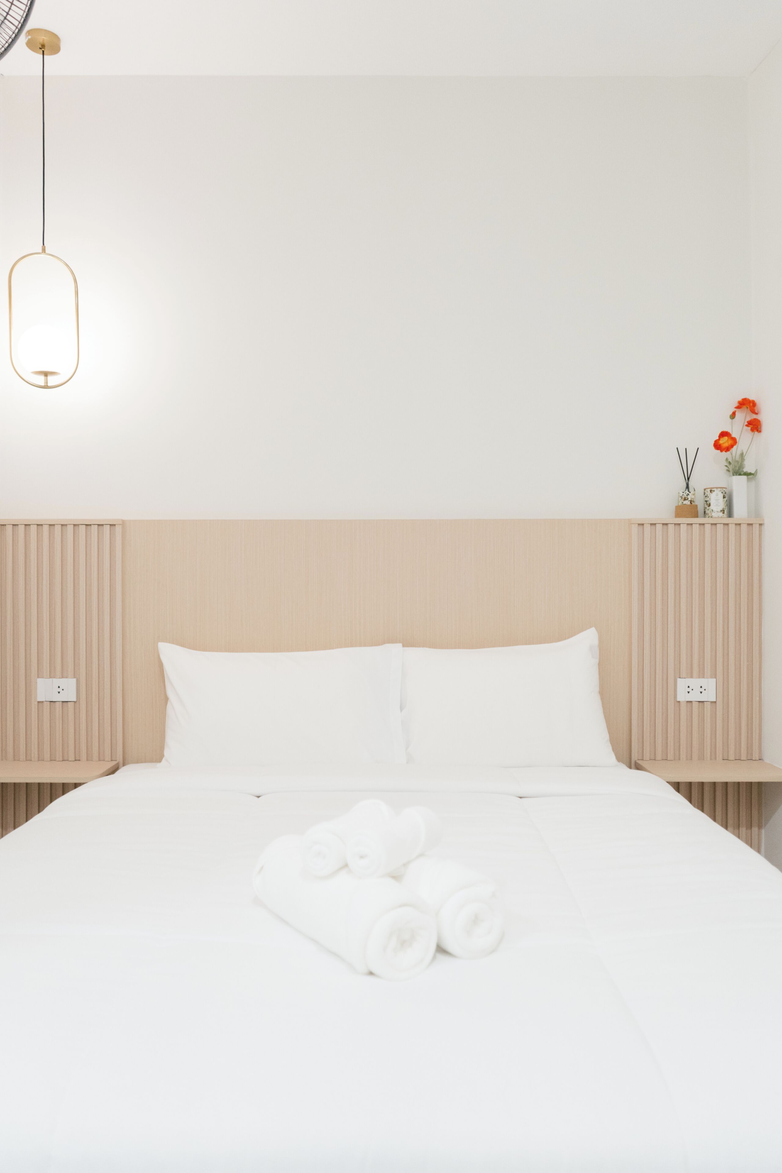 Cama bien hecha con sábanas blancas y toallas dobladas al frente.