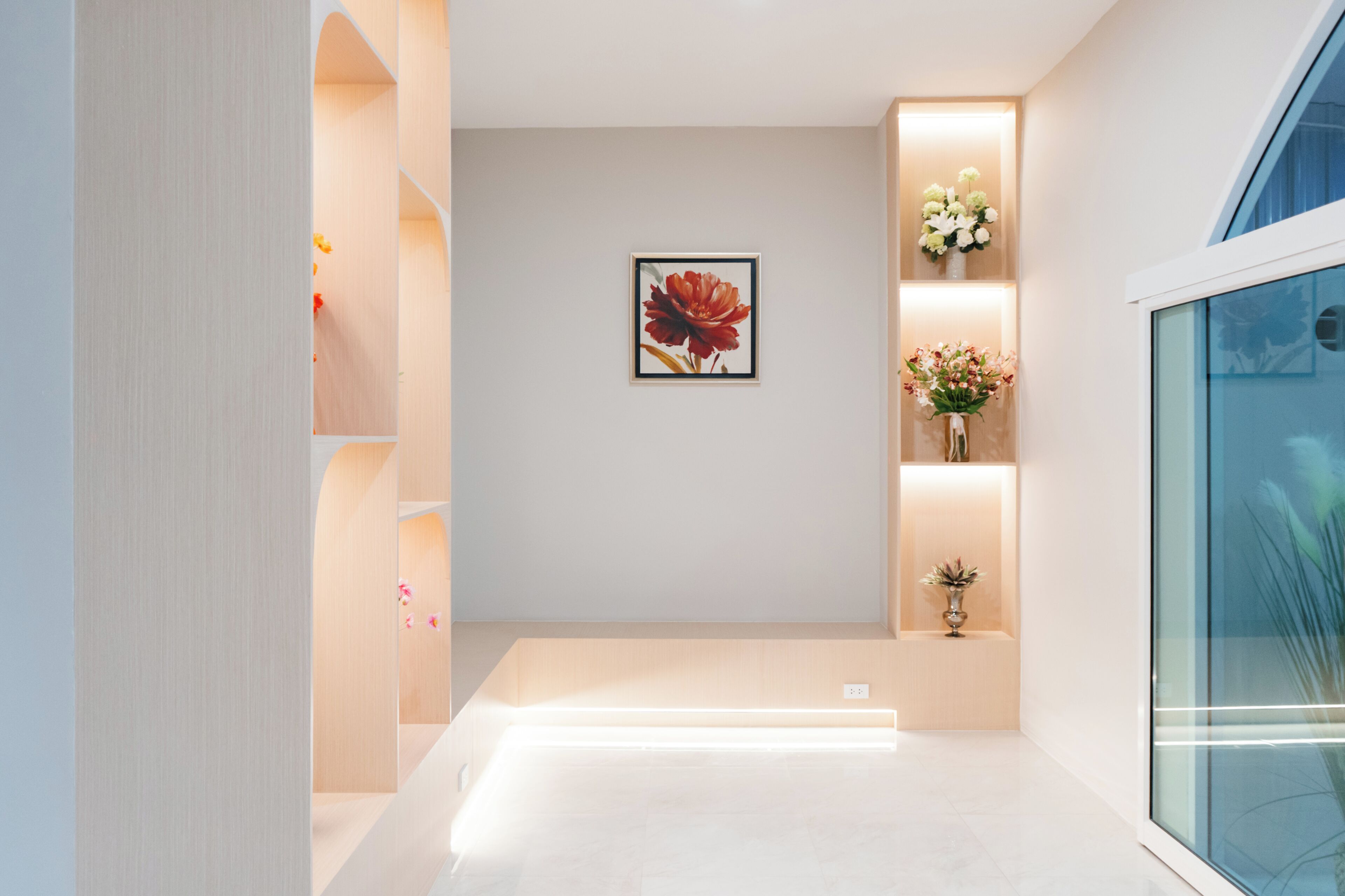 Un interior moderno con diseño minimalista, que presenta una obra de arte montada en la pared central, una serie de estanterías iluminadas y un panel de vidrio a la derecha.