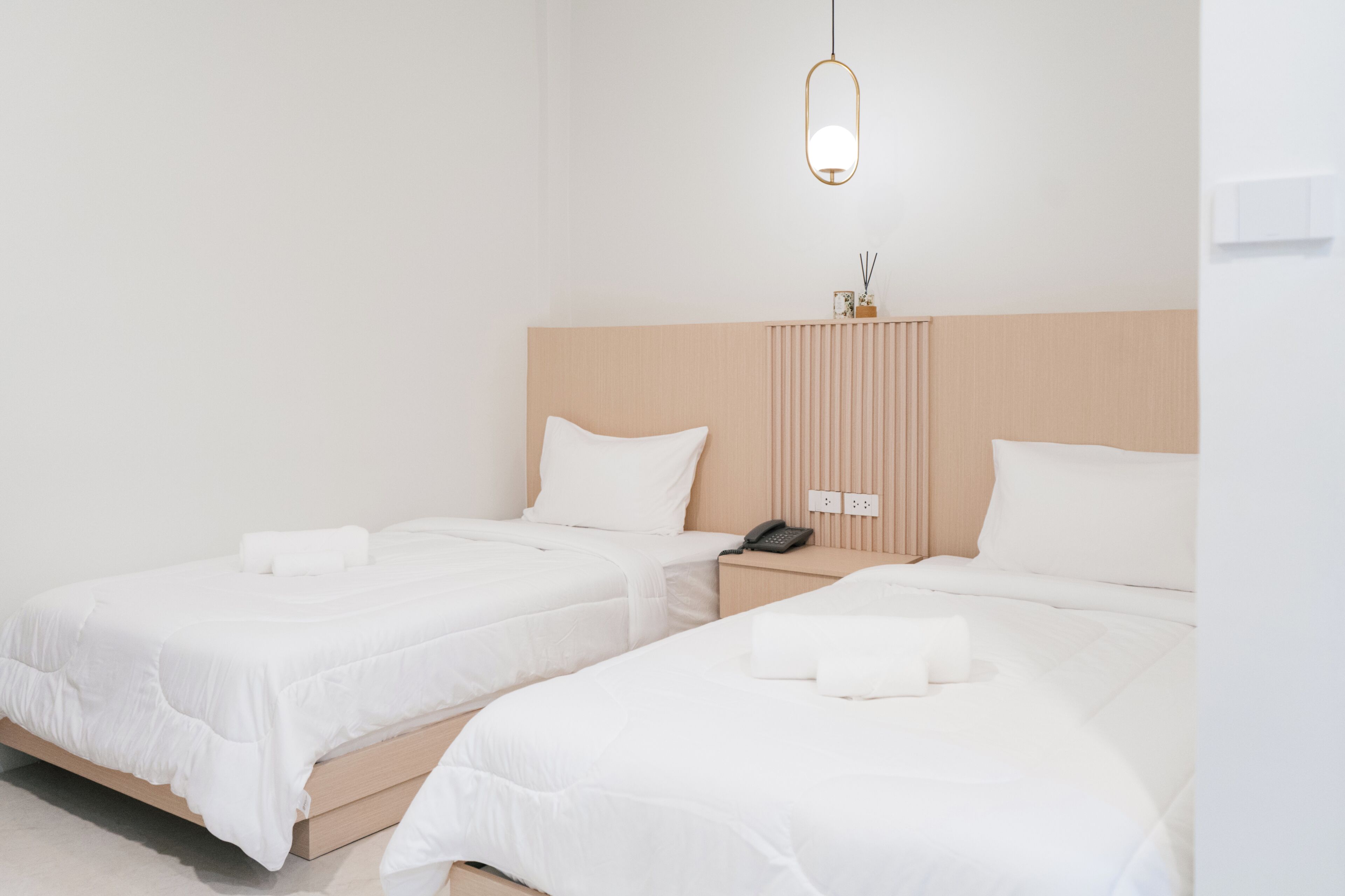 Habitación de hotel con dos camas individuales, cabecero de madera, mesita de noche con teléfono y lámpara colgante.