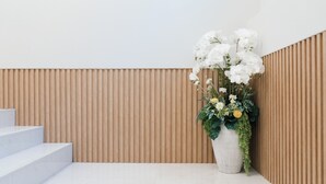 A modern interior with a white staircase, a wooden slatted wall, and a large white vase with flowers.