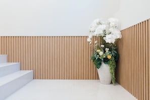 A modern interior with a white staircase, a wooden slatted wall, and a large white vase with flowers.