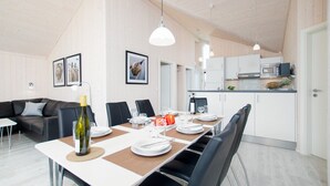 A modern dining area with a long table set for six, a sofa, and a kitchen in the background. - Haus mit Sauna im Zimmer (Grossenbrode)