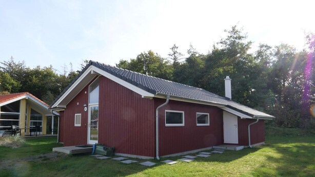 A red single-story house with a sloped roof, a front door, and a small porch area. - Haus mit Sauna im Zimmer (Grossenbrode)