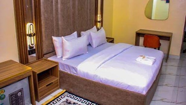 Una habitación de hotel con una cama, una mesita de noche de madera, un espejo y un escritorio con una silla.