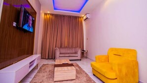 Una sala de estar moderna con un televisor de pantalla plana montado en la pared, un sofá, un sillón amarillo y una mesa de centro de madera.