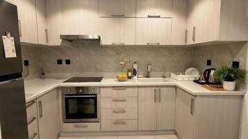Una cocina moderna con armarios de madera clara, electrodomésticos de acero inoxidable y piso de baldosas.